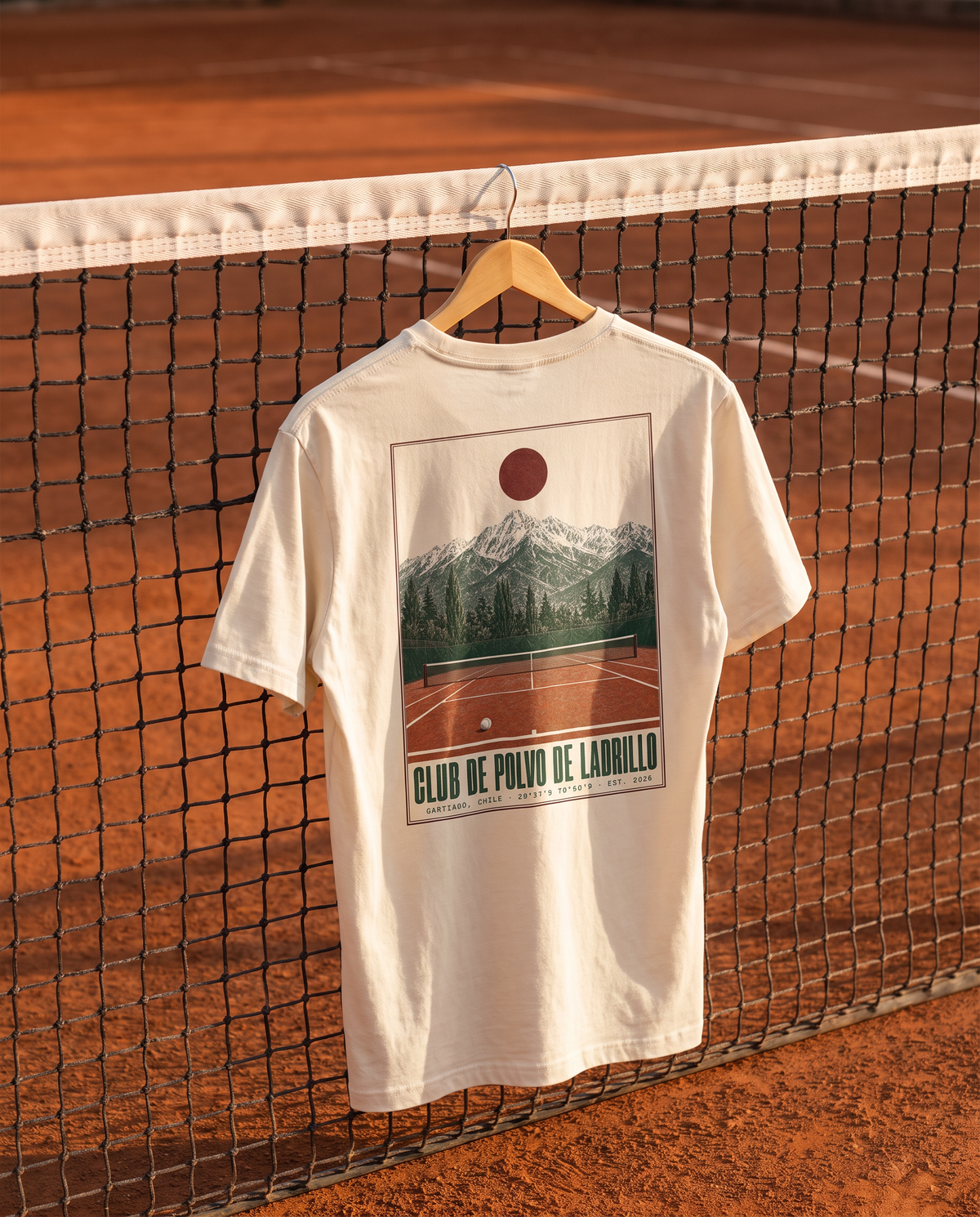 Polera Club de Polvo de Ladrillo beige colgada en la red de una cancha de tenis al atardecer