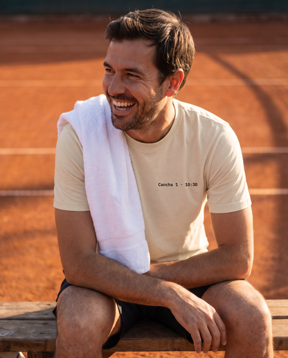 Tenista con la polera Match Summary color Beige de frente, calce clásico, junto a una cancha de polvo de ladrillo