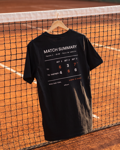 Polera de tenis Match Summary color Negro colgada en la red de una cancha de polvo de ladrillo