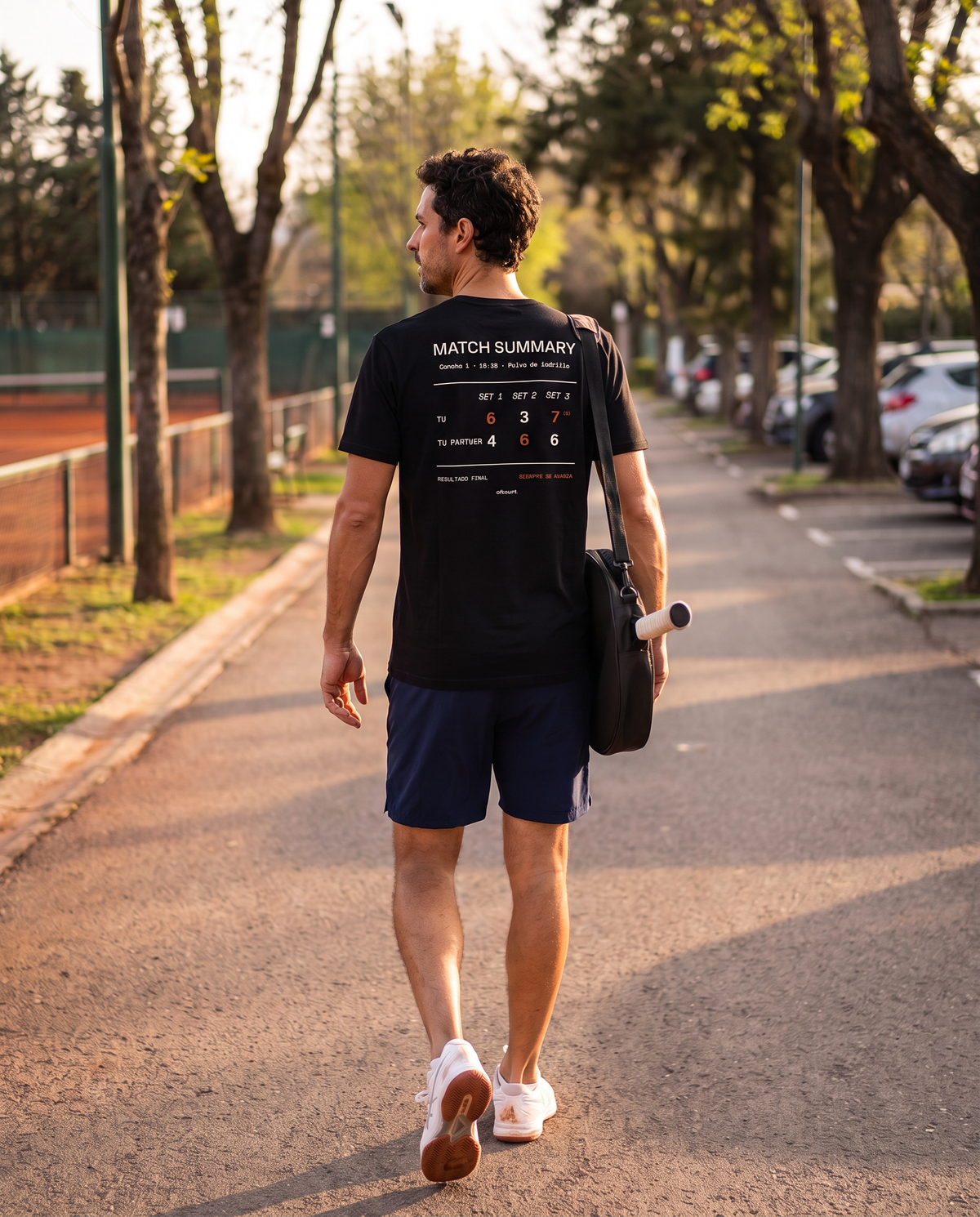 Tenista con la polera Match Summary color Negro caminando con su bolso junto a las canchas de polvo de ladrillo