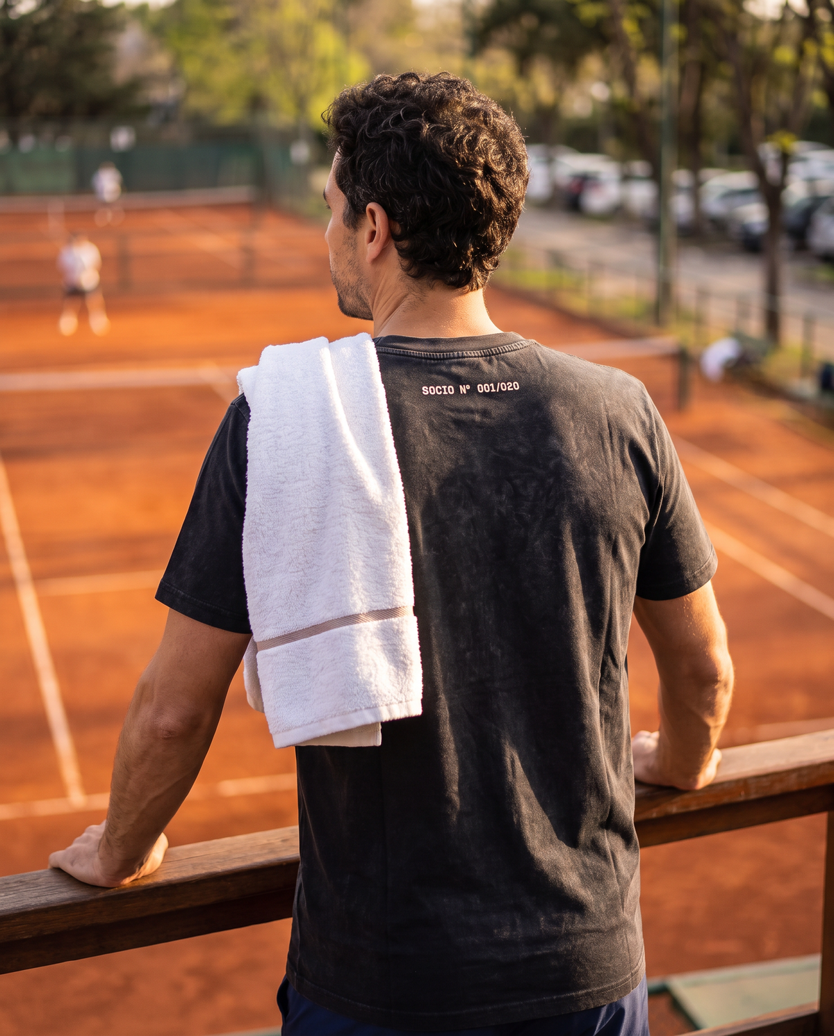Tenista de espaldas con la polera Socio Nº color Negro numerada en la nuca mirando las canchas de polvo de ladrillo