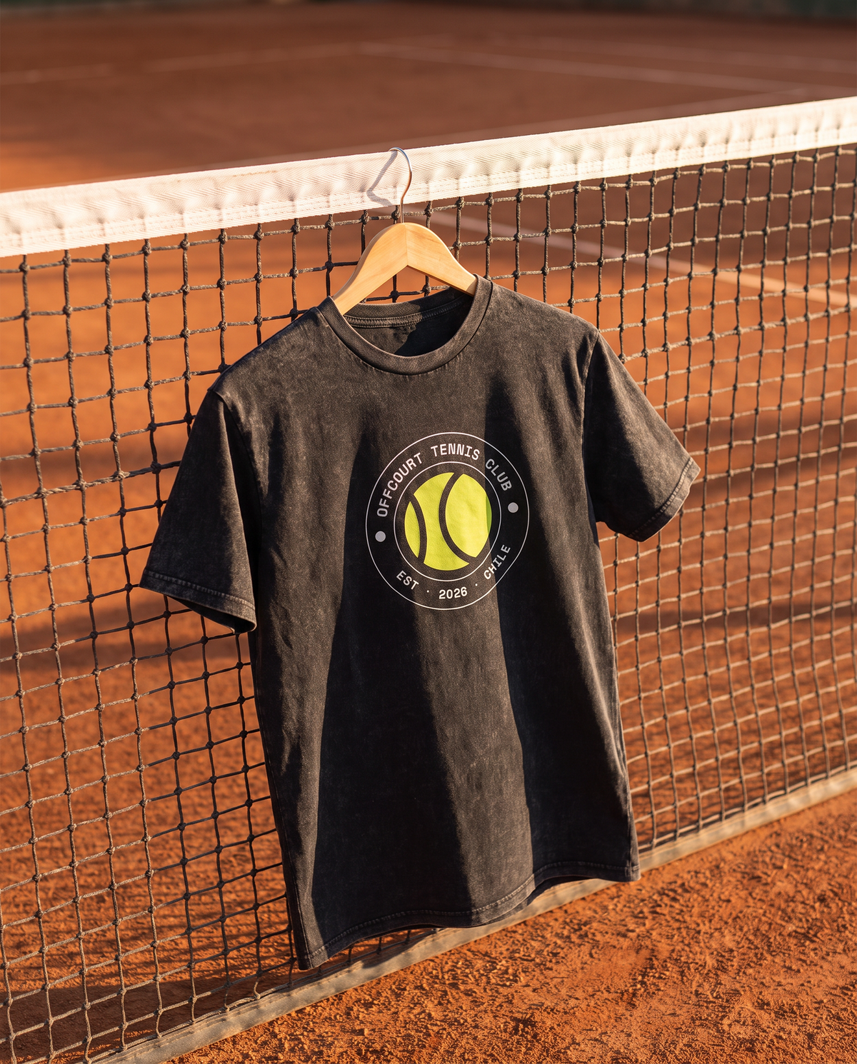 Polera acid wash Socio Nº de offcourt. color Negro colgada en la red de una cancha de polvo de ladrillo