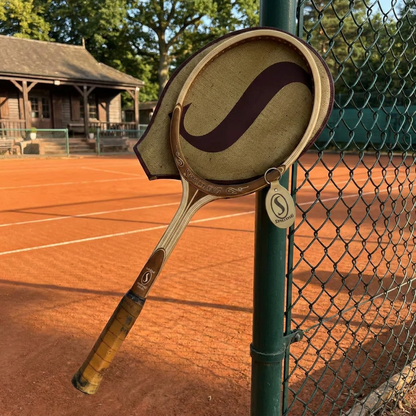 Raqueta Spalding Natural apoyada en la malla de una cancha de arcilla